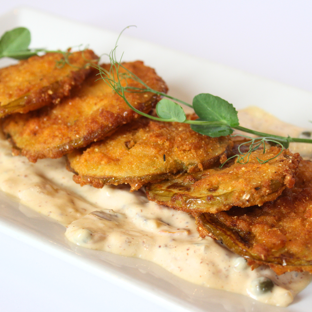Fried green tomatoes on a bed of creamy sauce, garnished with pea shoots, served on a white plate.