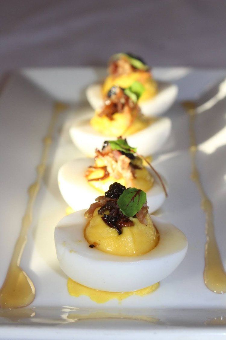 Deviled eggs with yellow filling, topped with garnish, arranged on a white plate with drizzled sauce.