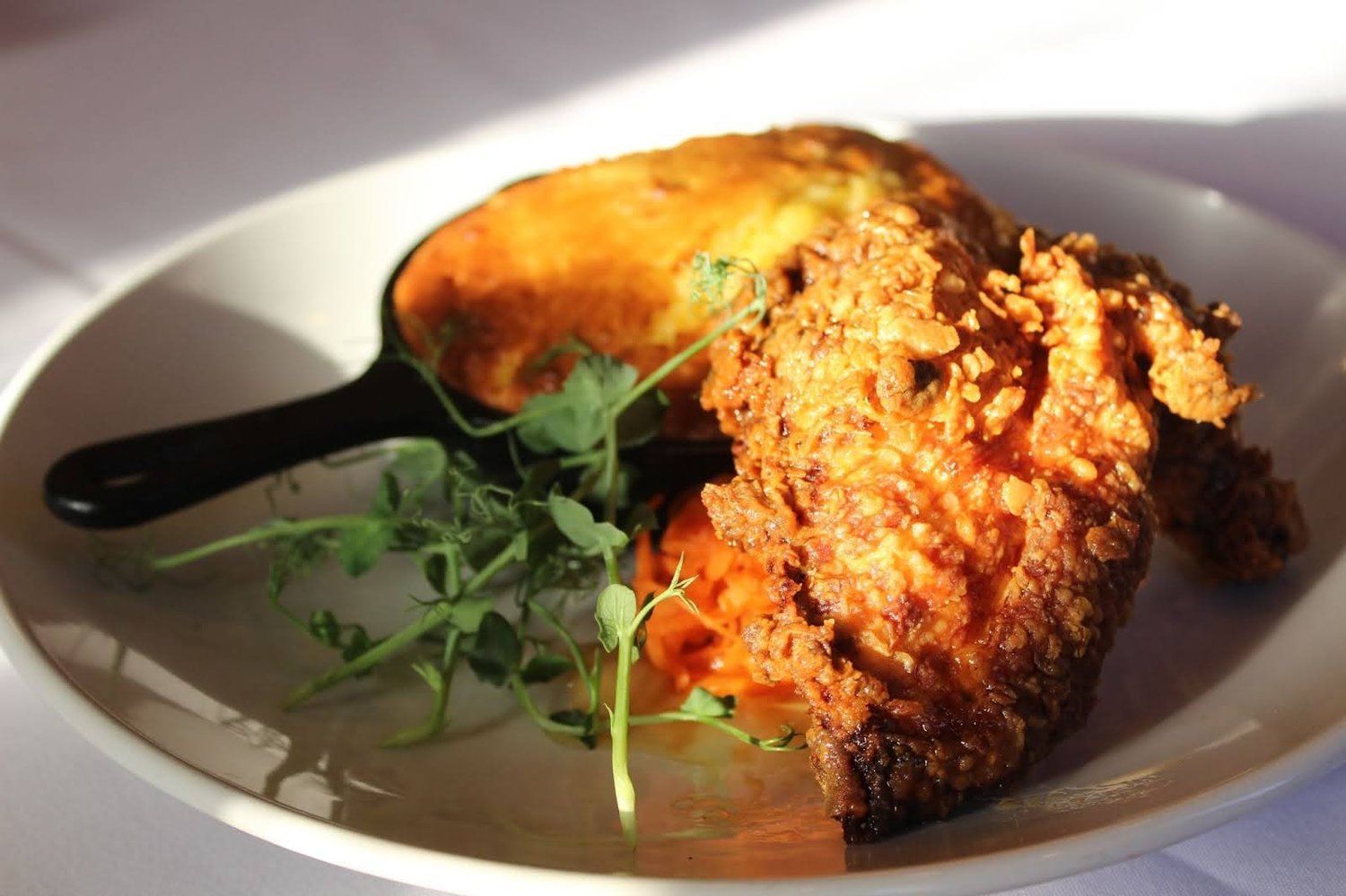 Fried chicken wing on a white plate with mashed sweet potato and microgreens.