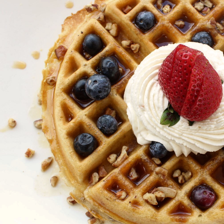 Waffle topped with blueberries, whipped cream, strawberry, pecans, and syrup.