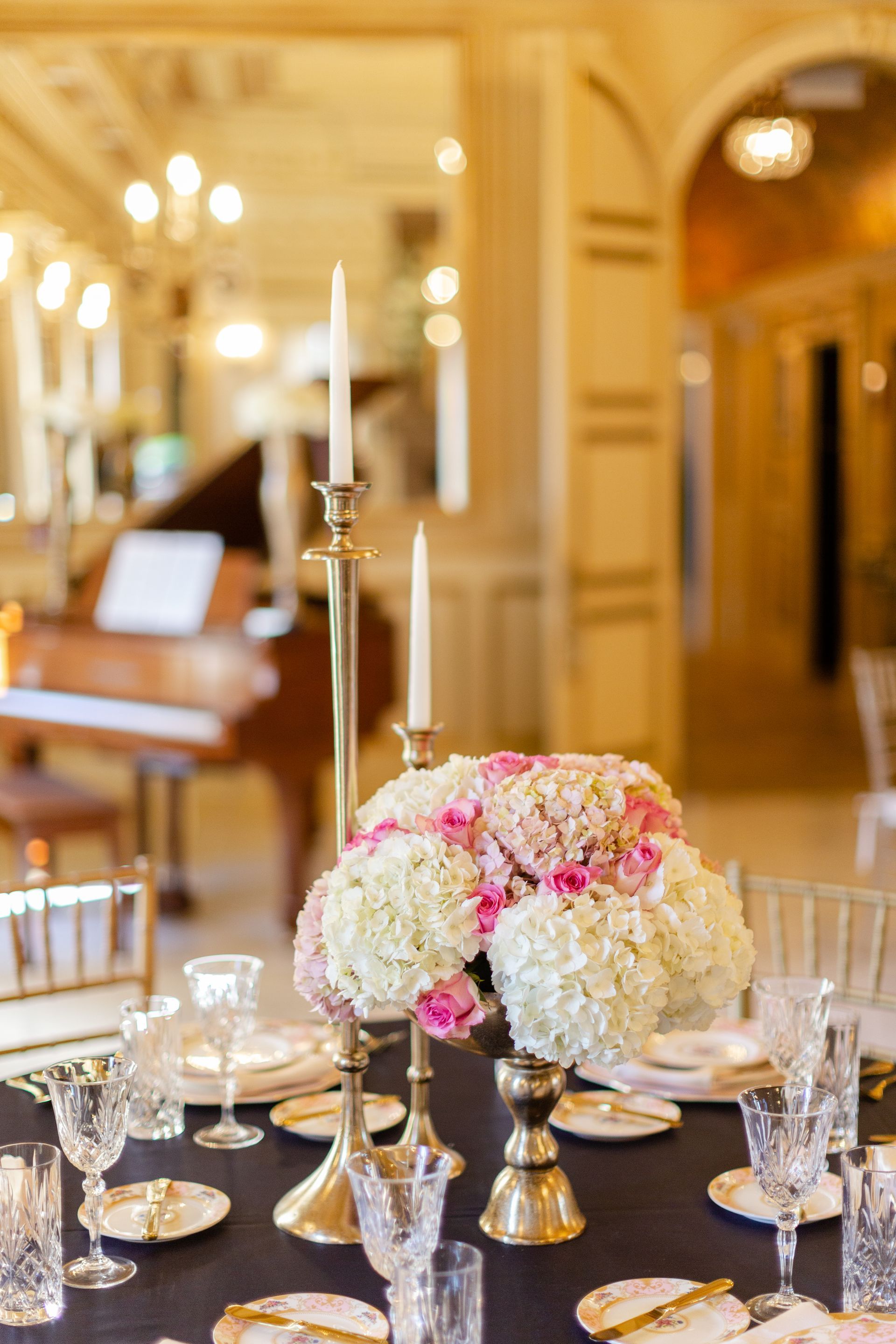 Elegant table setting with flowers, gold candle holders, and a piano in the background.