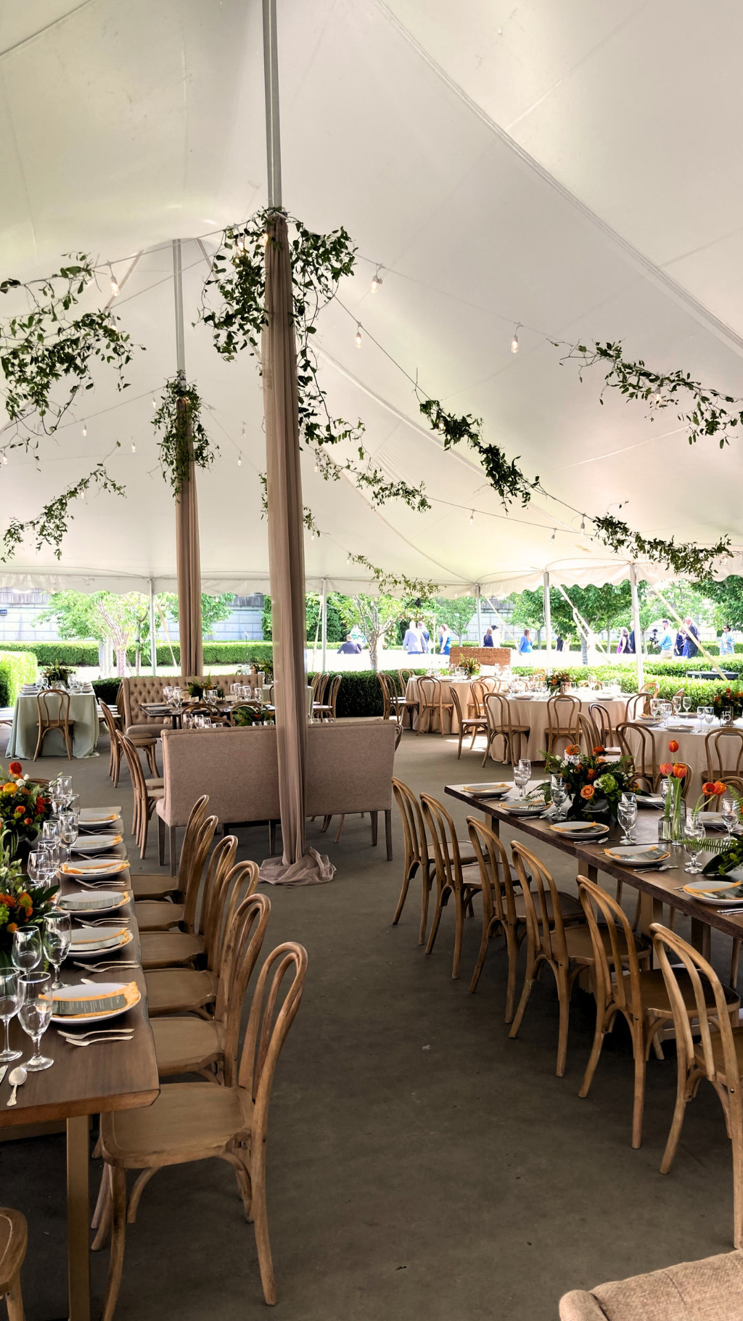 Wedding reception tent with tables set for guests, decorated with greenery and lights.