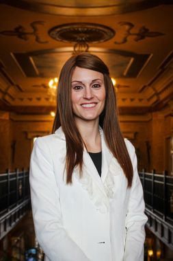 Woman in white blazer smiles in ornate interior.