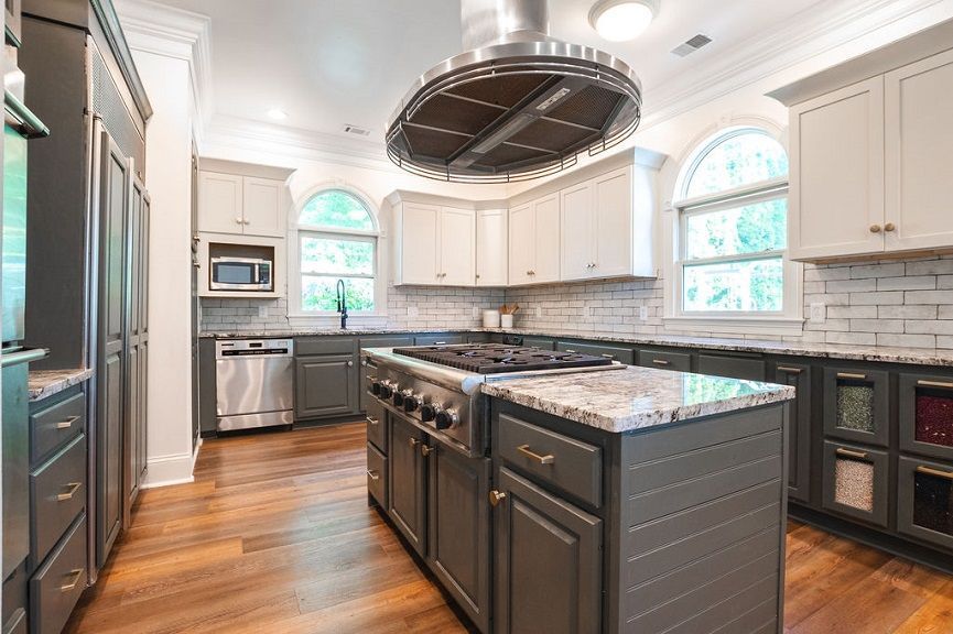 Modern kitchen with gray island and white cabinets. Stainless steel appliances, hardwood floors, and arched windows.