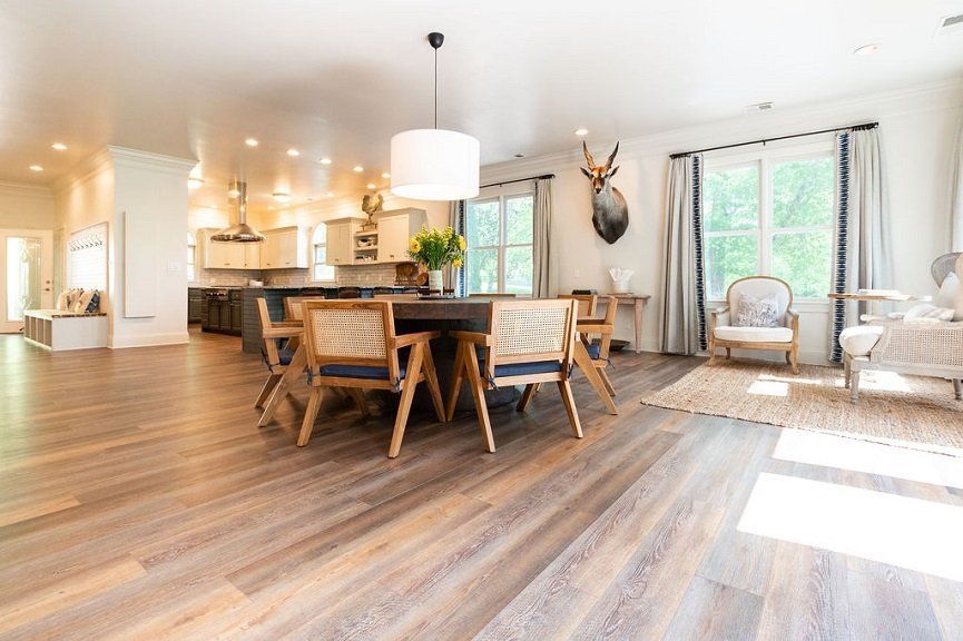 Open-concept dining and kitchen area with wood floors. Features a dining table with woven chairs, and a deer head wall decor.