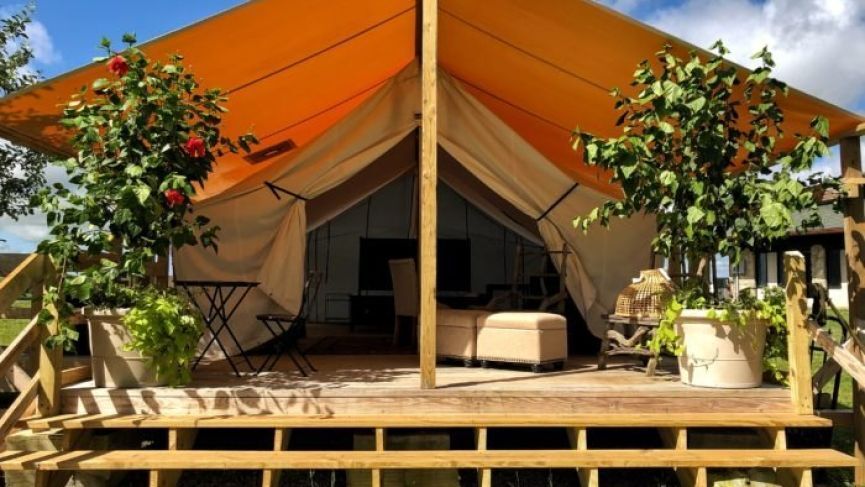 A glamping tent with an orange canopy, wooden deck, potted plants, and a small table.