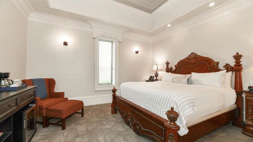 Ornate bedroom with a large wooden bed, armchair, and dresser.