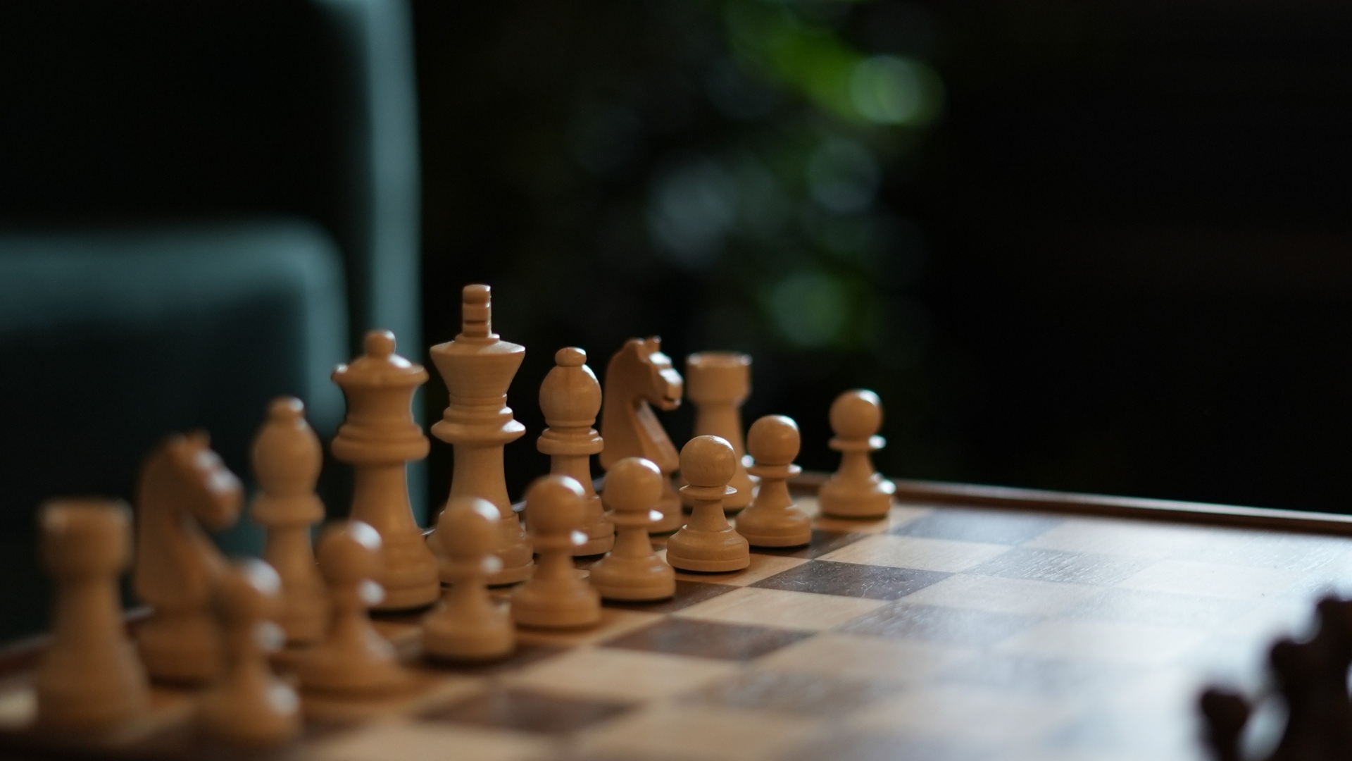 Chess pieces arranged on a chessboard, in a low light setting.