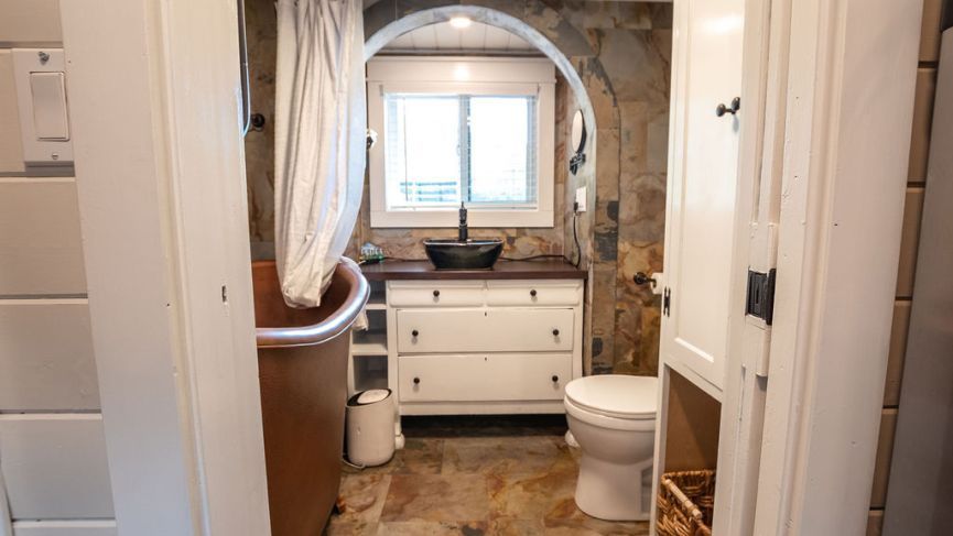 Bathroom with a stone arched doorway, copper tub, white vanity, and a window.