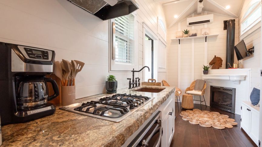 Cozy tiny home kitchen with granite countertop, stovetop, coffee maker, and fireplace.