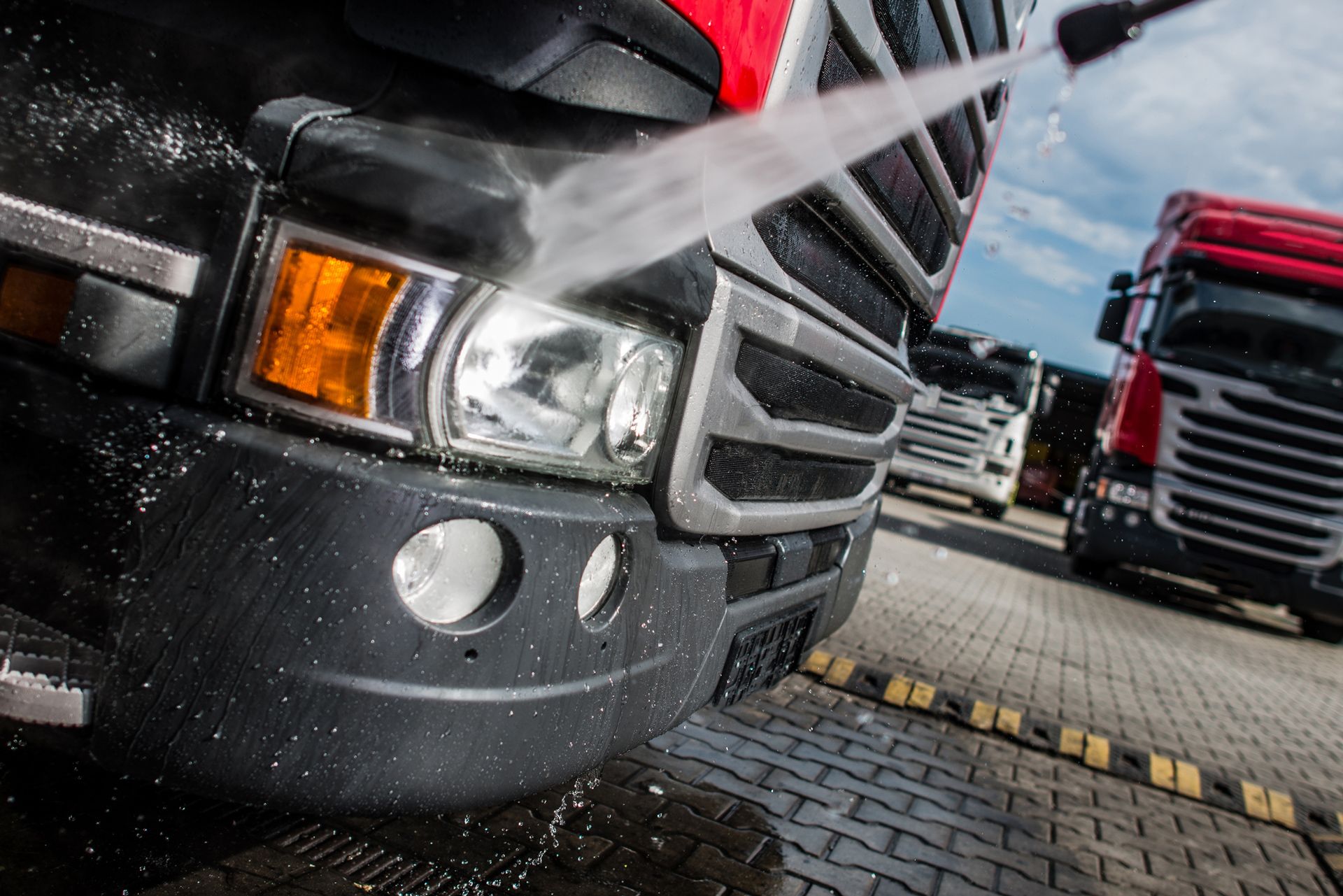 Washing the front of a semi-truck with water; other trucks in background.