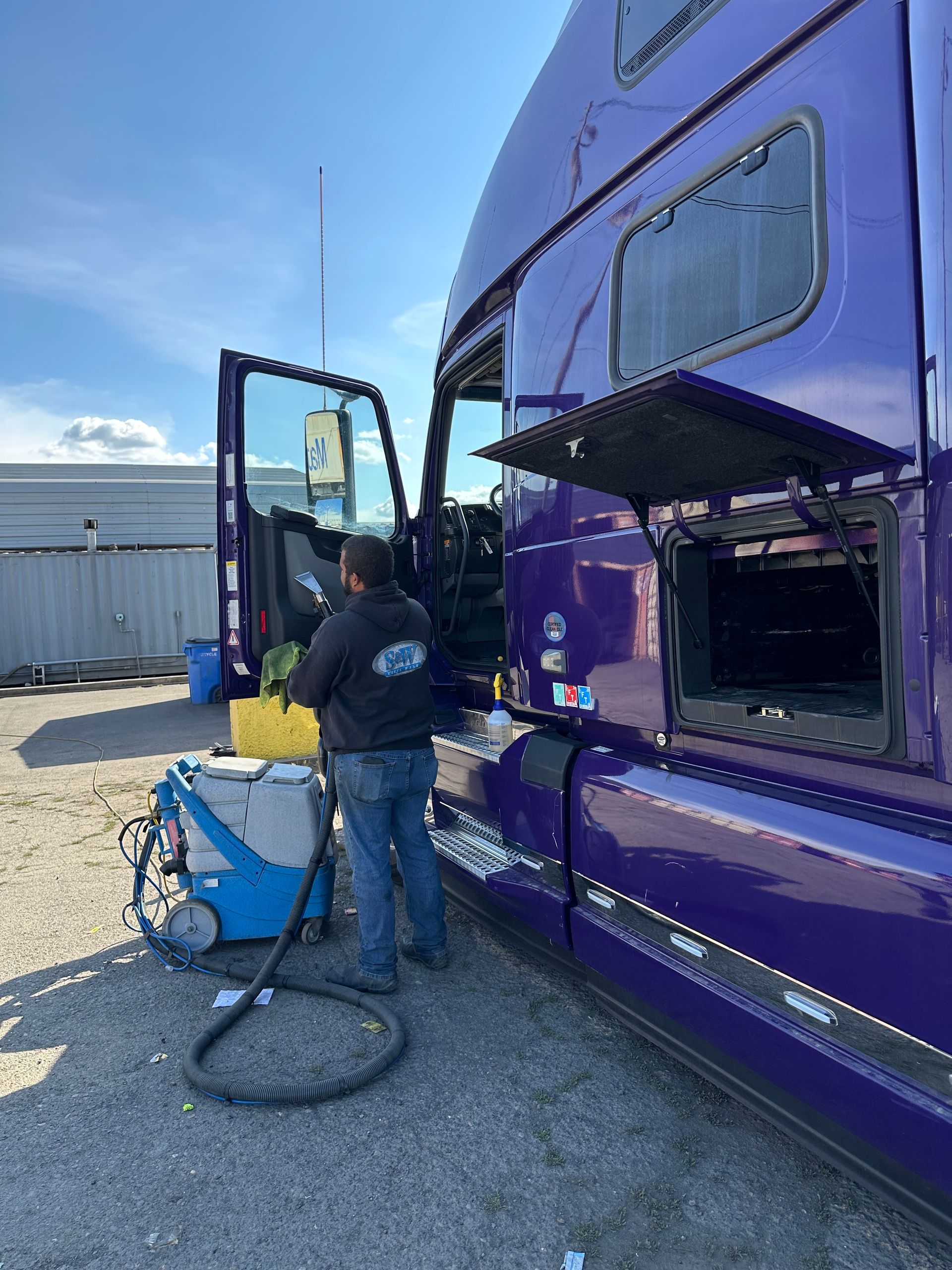 Man in cap and sunglasses pressure washing a red vehicle.