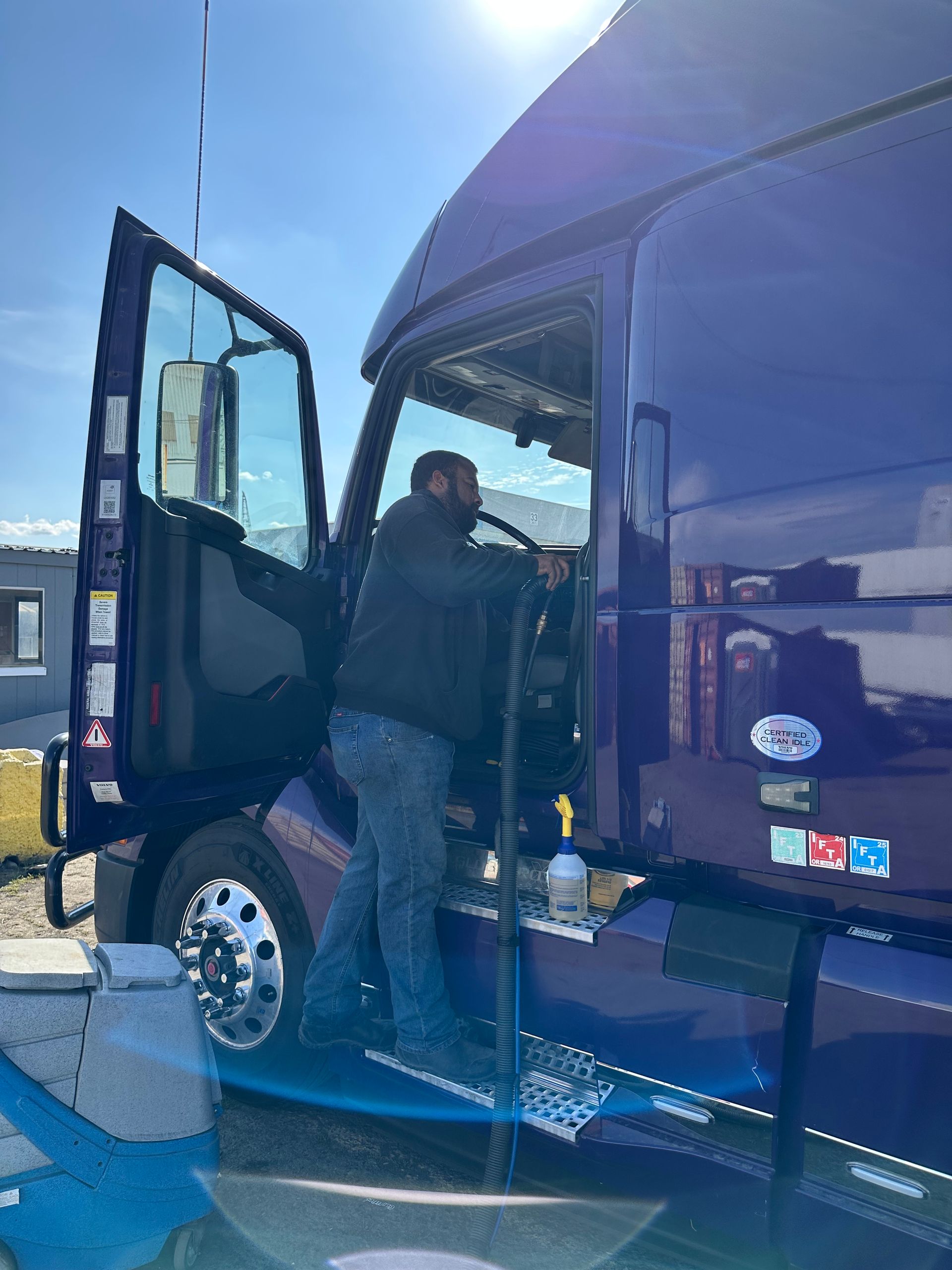 Person power washing a tow truck; white vehicle, concrete surface.