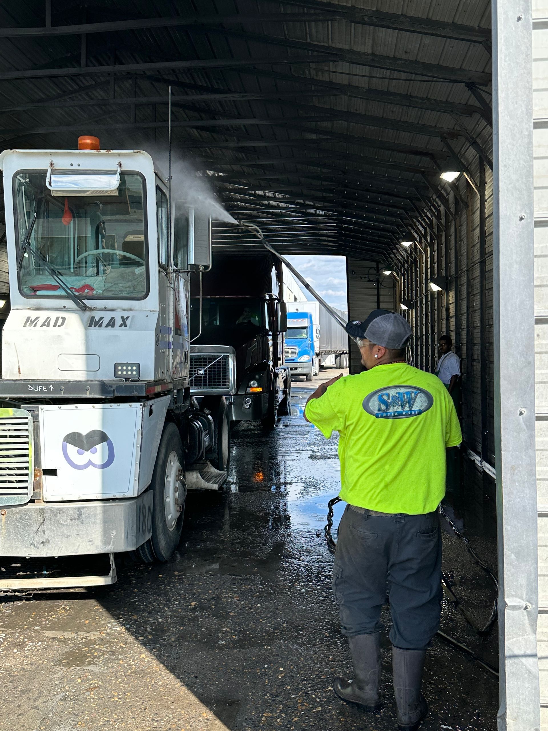 White truck being washed with a pressure washer; the front grill is being sprayed. Outdoors, sunny day.