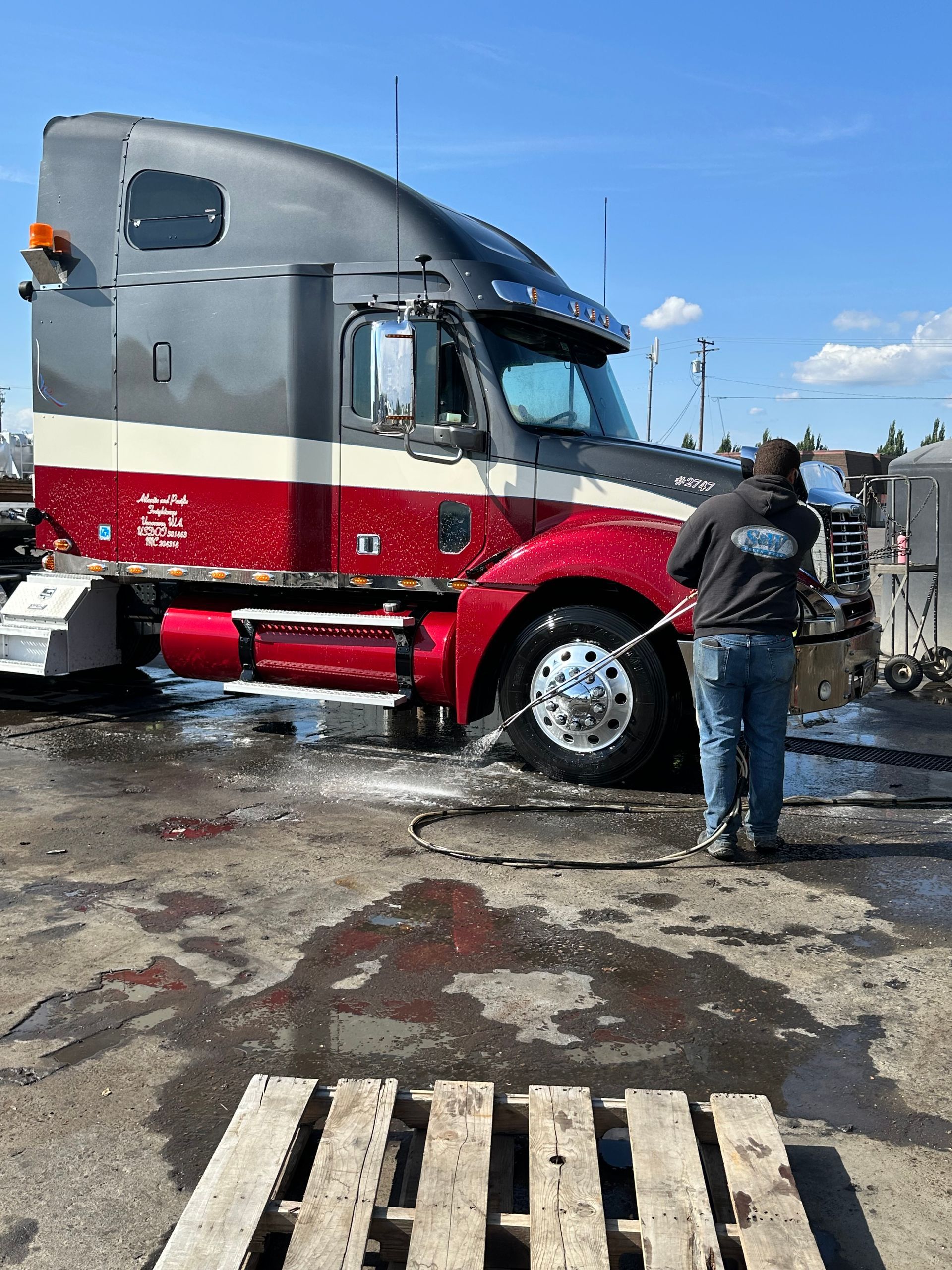 White semi-truck with open hood being worked on inside a gray building.