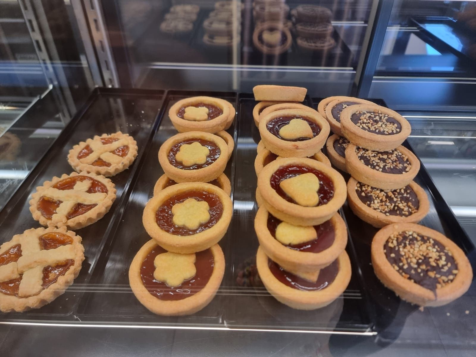 Vetrina con varie crostate rotonde con marmellata, cioccolato e pasticcini.