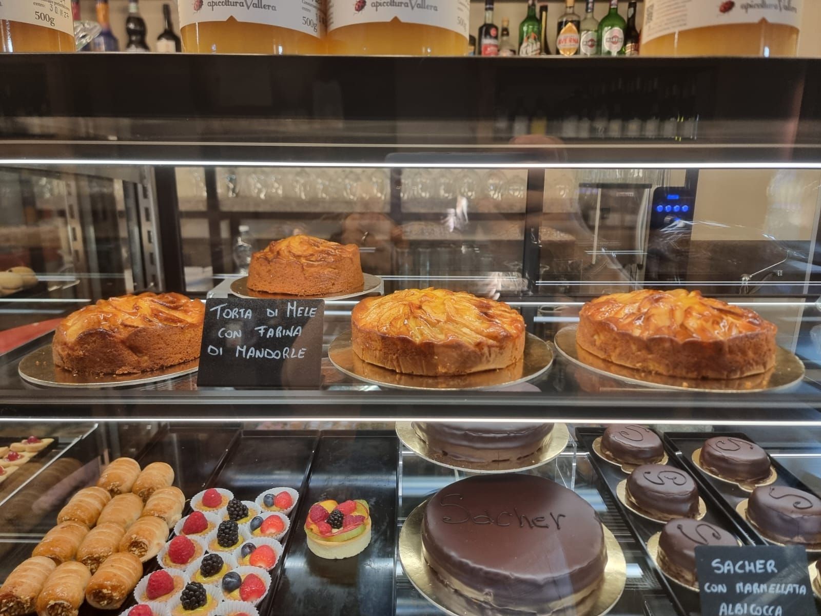Vetrina con vari tipi di pasticceria: torte, crostate e cannoli. Colori marrone chiaro e cioccolato, ambientazione da pasticceria.