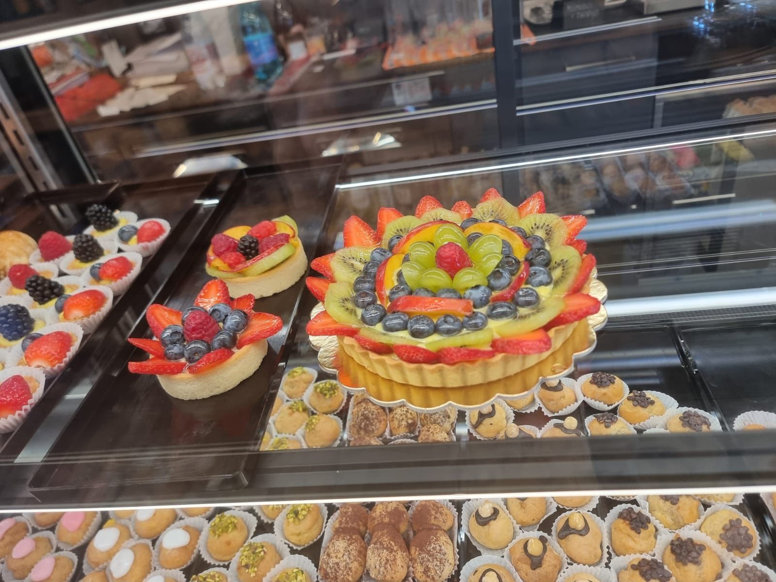 Pasticcini esposti in una vetrina da pasticceria, con crostate di frutta con frutti di bosco e kiwi.