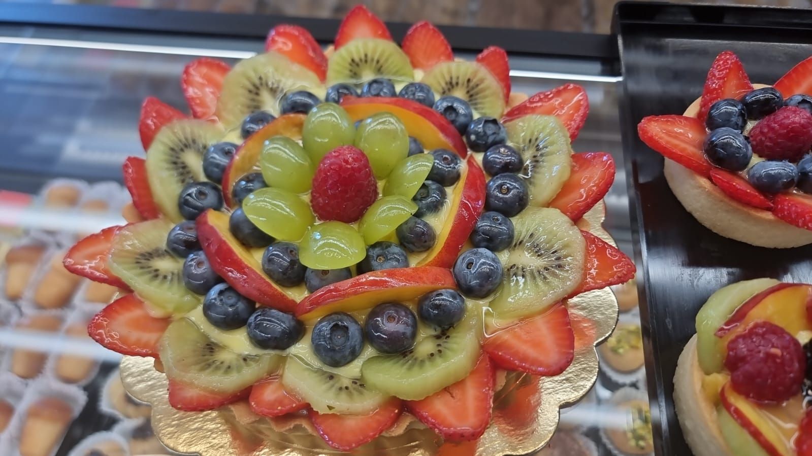 Crostata di frutta decorata con fragole, kiwi, mirtilli, uva e un lampone.