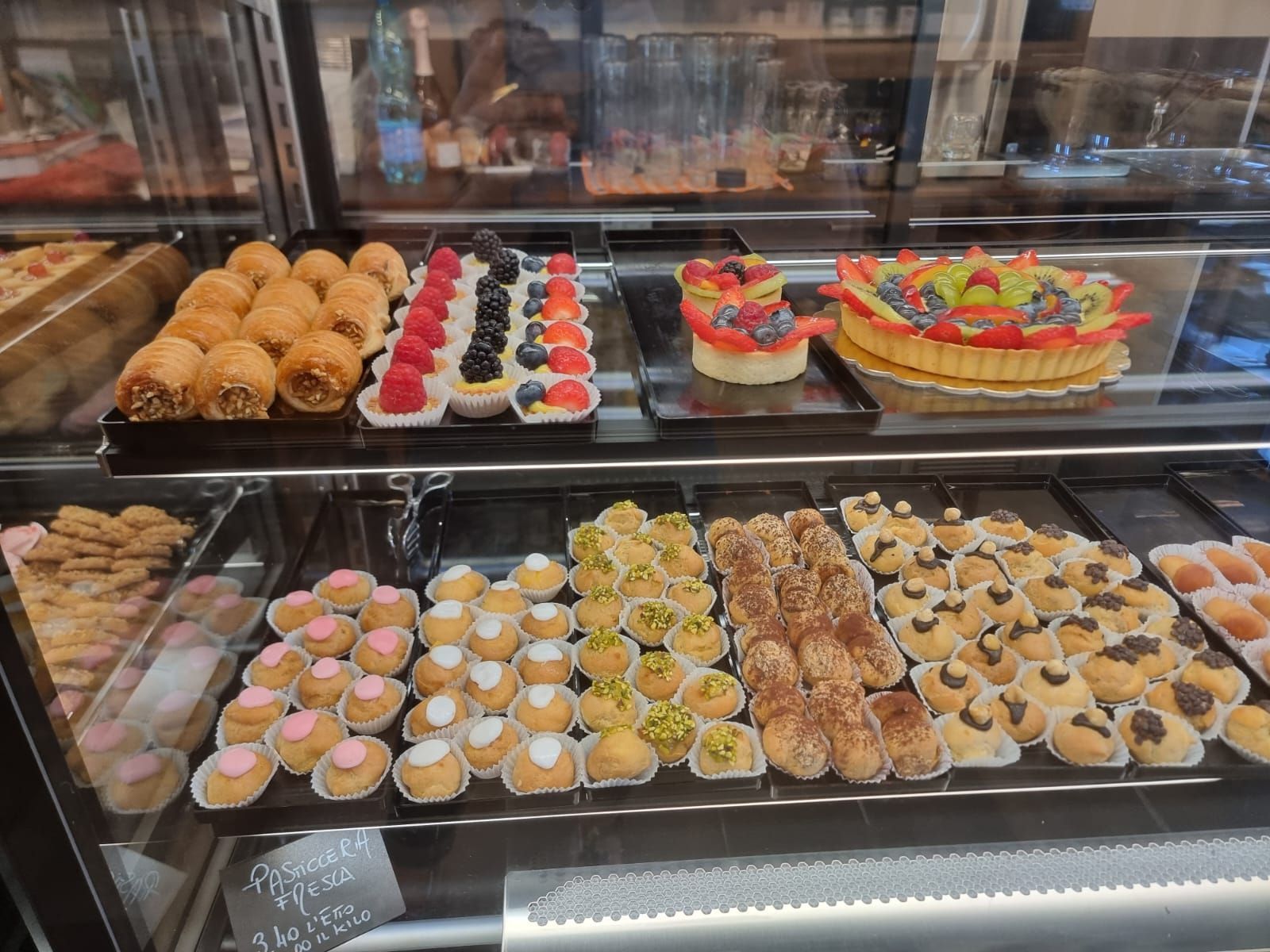 Pasticcini esposti in una vetrina di vetro, tra cui crostate di frutta e biscotti assortiti.