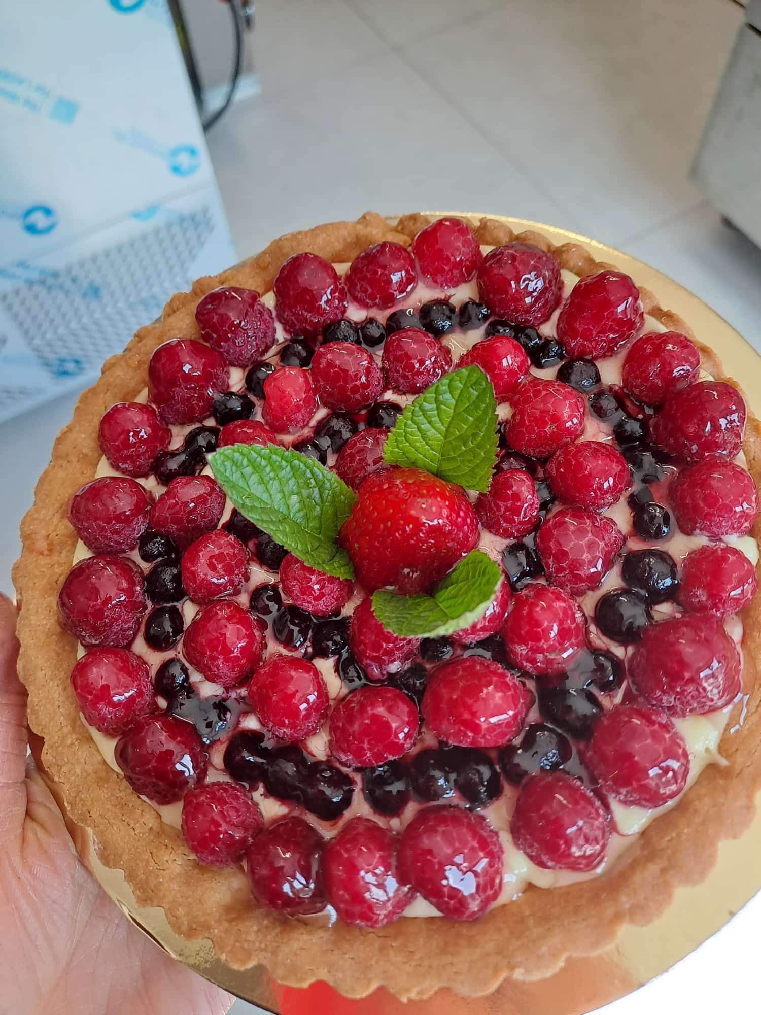 Crostata ai frutti di bosco con lamponi, mirtilli, fragole e menta su una crosta dorata. Servita da una persona.