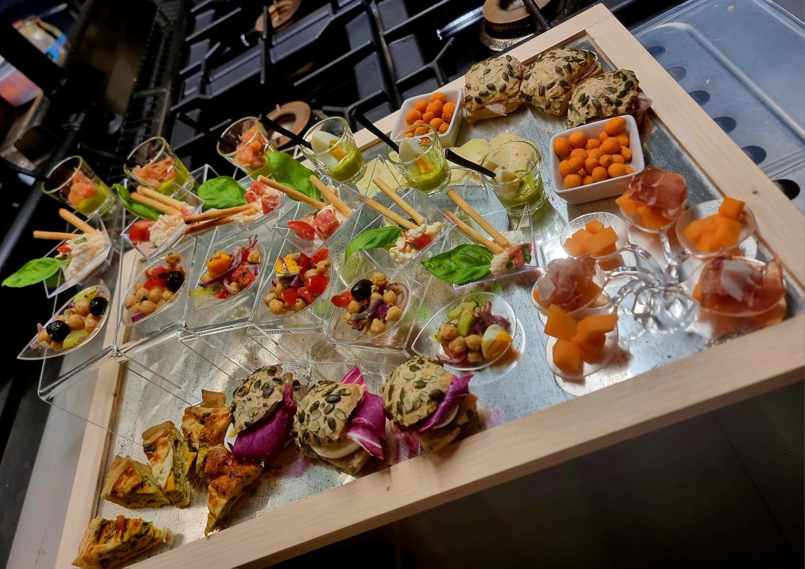 Antipasti assortiti su un vassoio, con mini-piatti colorati con vari ingredienti e consistenze, in un ambiente da cucina.