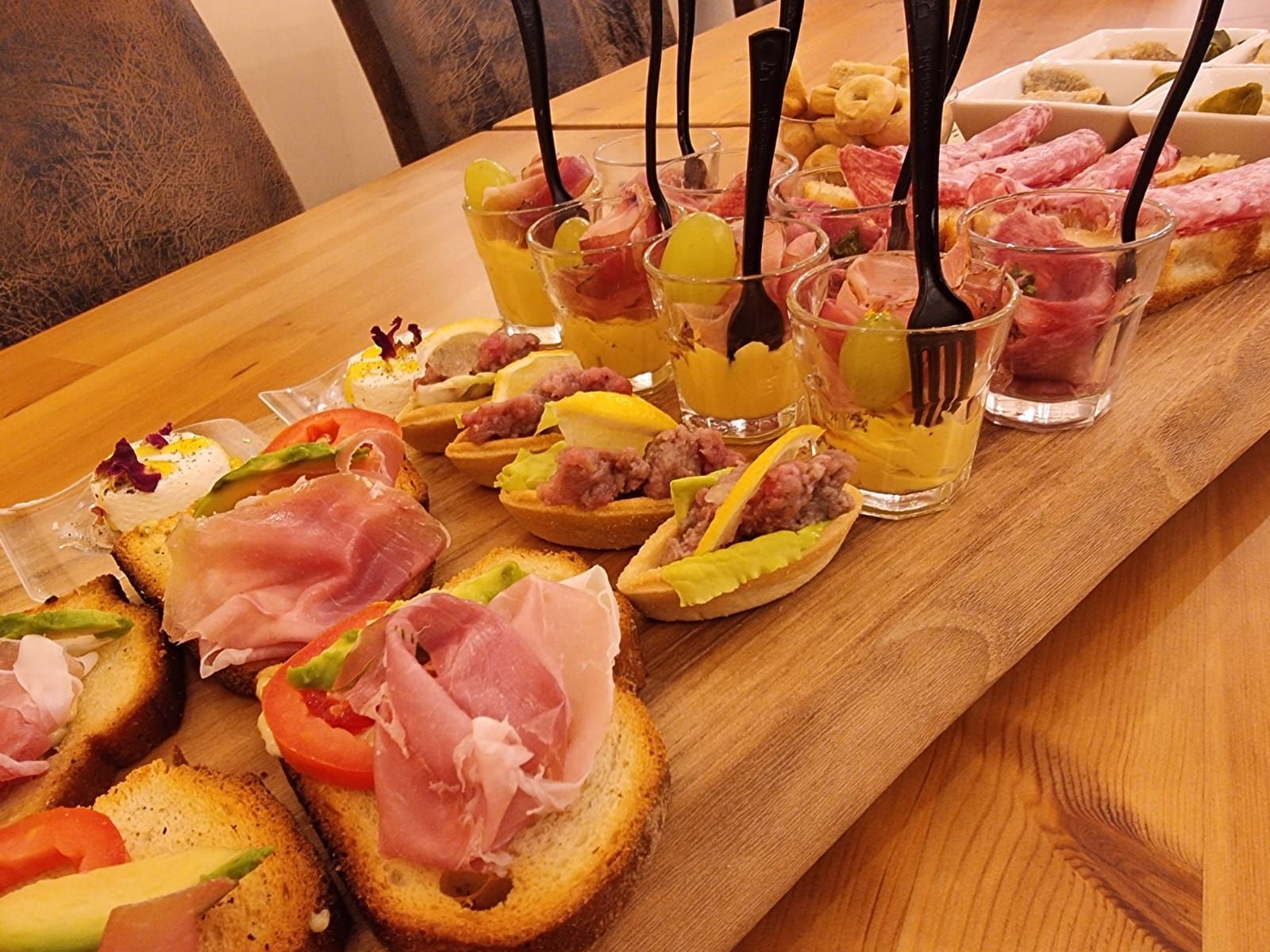 Tagliere di legno con vari antipasti: bruschette, tortine e mini-cocktail, alcuni con forchette nere.