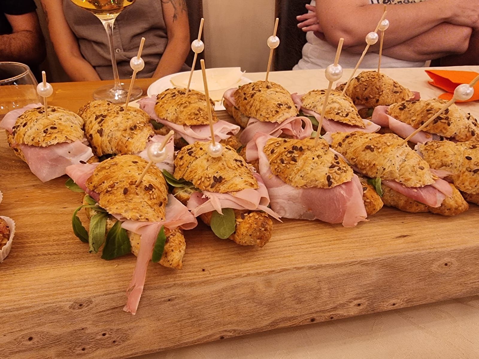 Piccoli panini su un tagliere di legno con prosciutto, rucola e stuzzicadenti.
