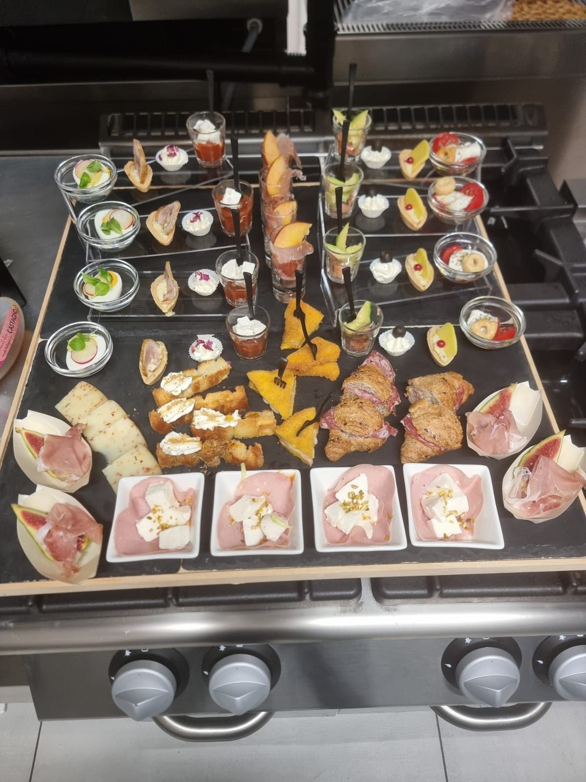 Una serie di antipasti disposti su una lavagna sopra un fornello. Vari piccoli piatti con cibo.