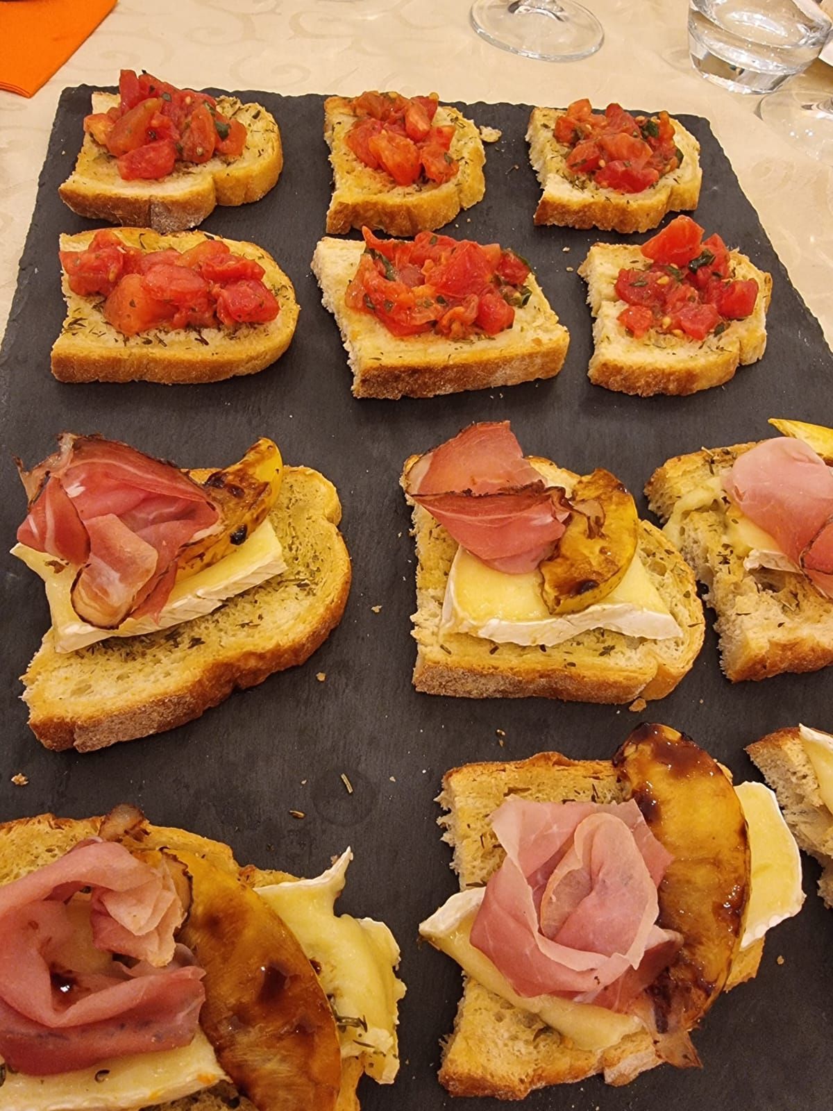 Bruschetta con pomodoro, prosciutto e brie su un vassoio di ardesia.