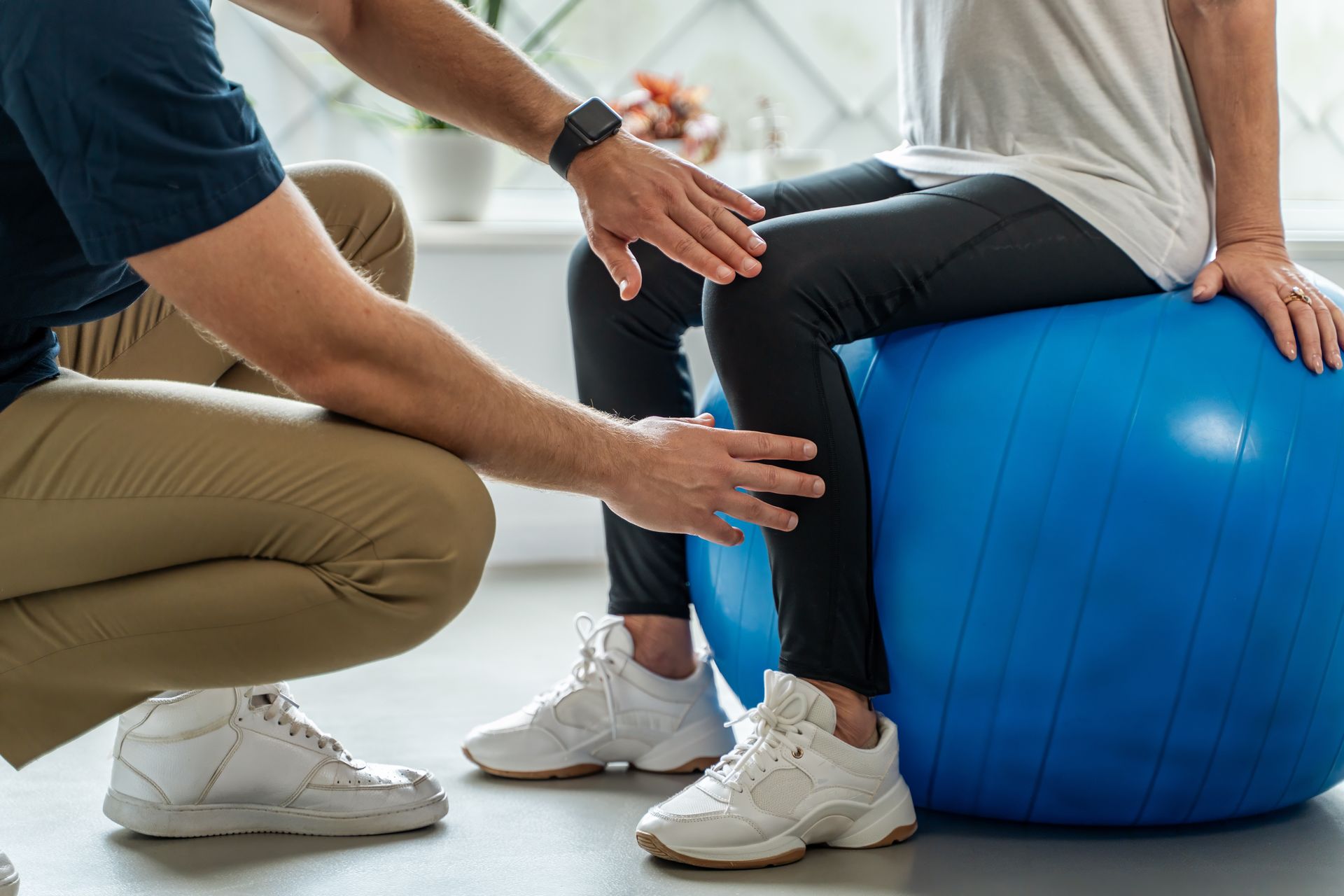Physical therapist assisting seated patient with exercise ball and leg stretch in a bright clinic