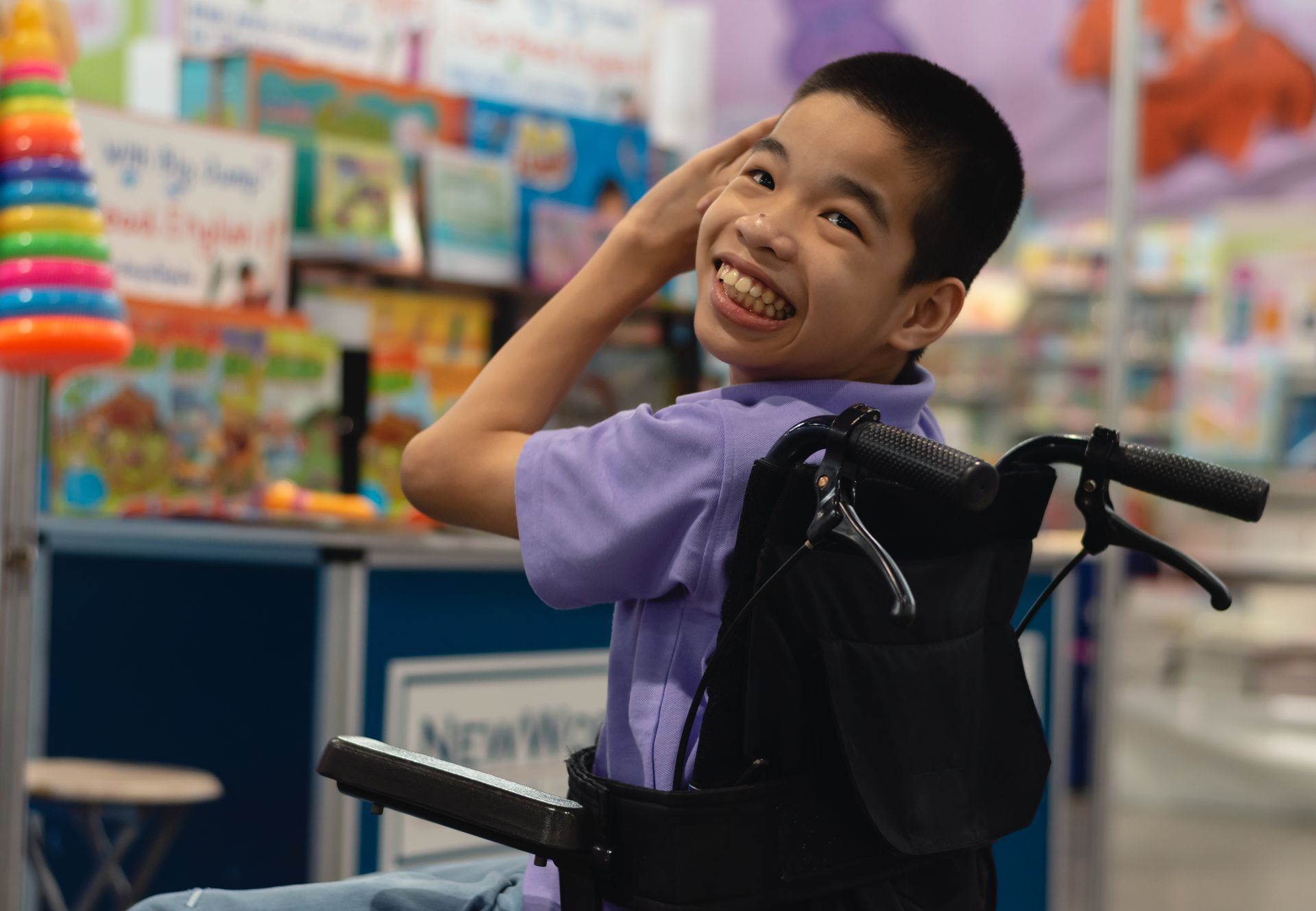 Smiling child in a wheelchair at a colorful toy store, wearing a purple shirt