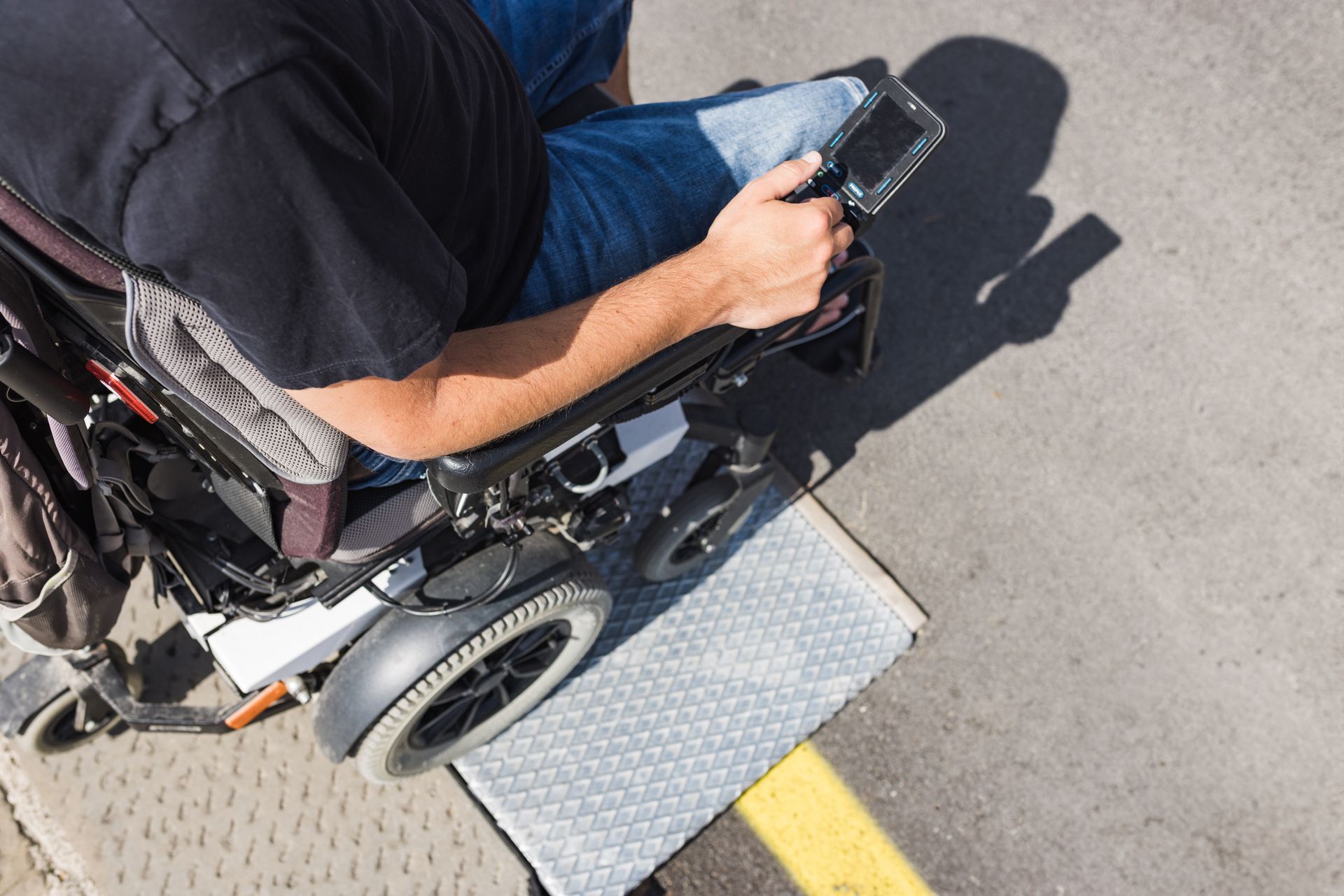 Person in a wheelchair using a smartphone on a curb beside a yellow line