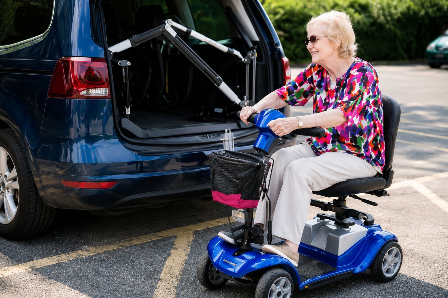 Person in a blue mobility scooter loading a wheelchair into the back of a dark van outdoors