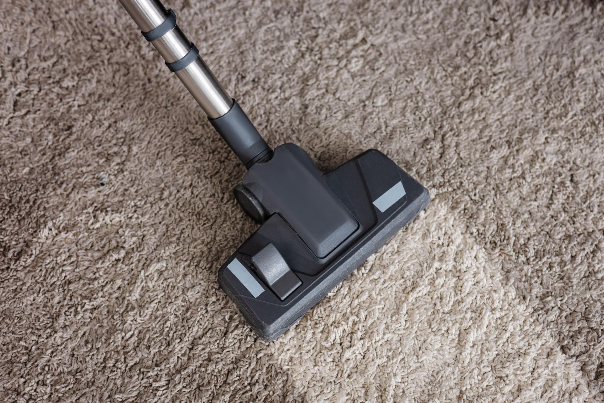 Vacuum cleaner head cleaning a light brown carpet.