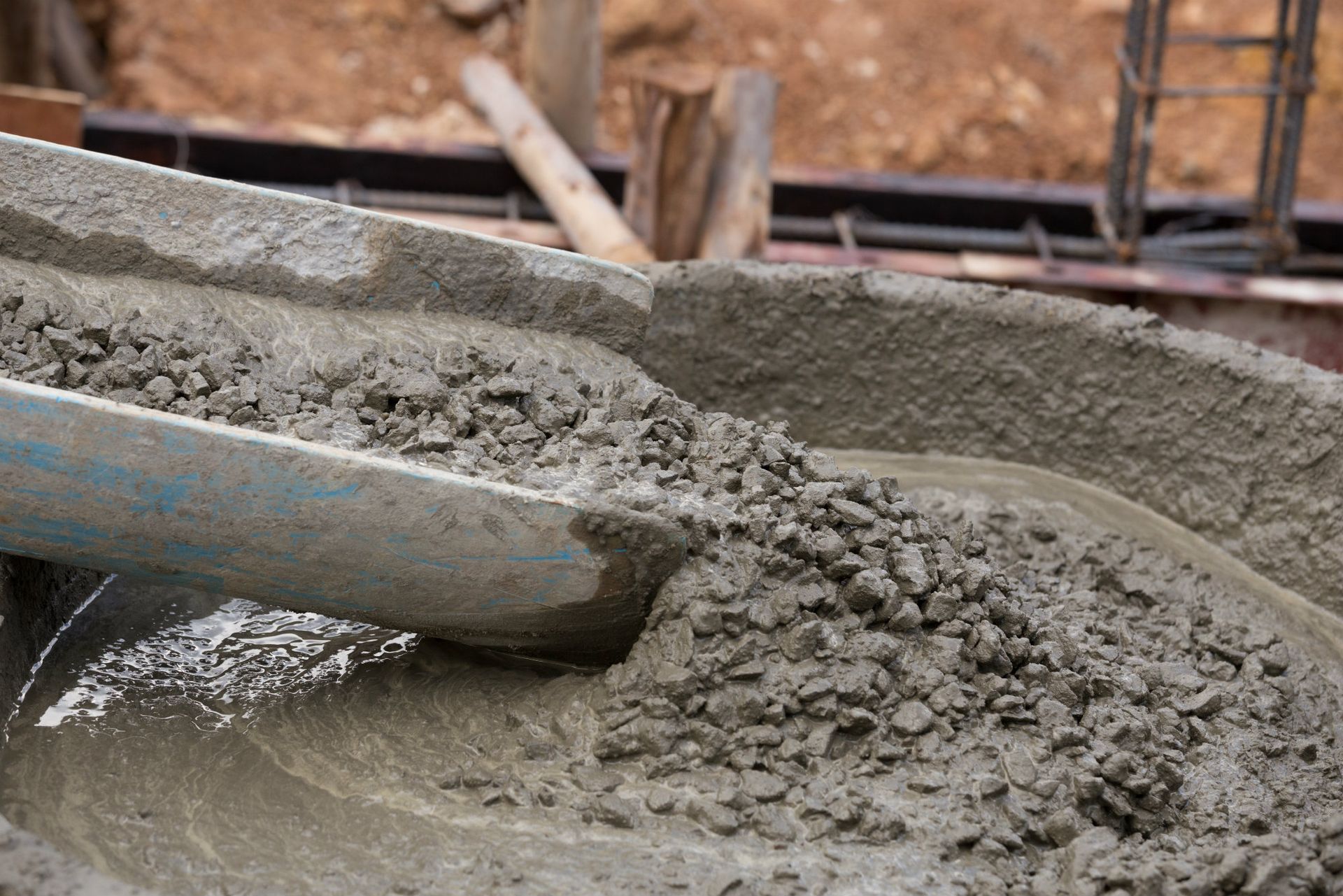 A construction worker wearing orange gloves is pouring concrete on a construction site.
