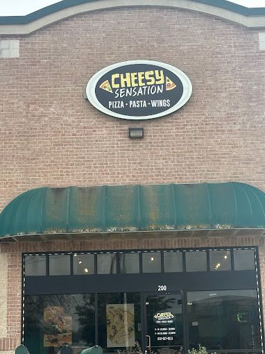 The front of a cheesy sensation pizza restaurant with a green awning.