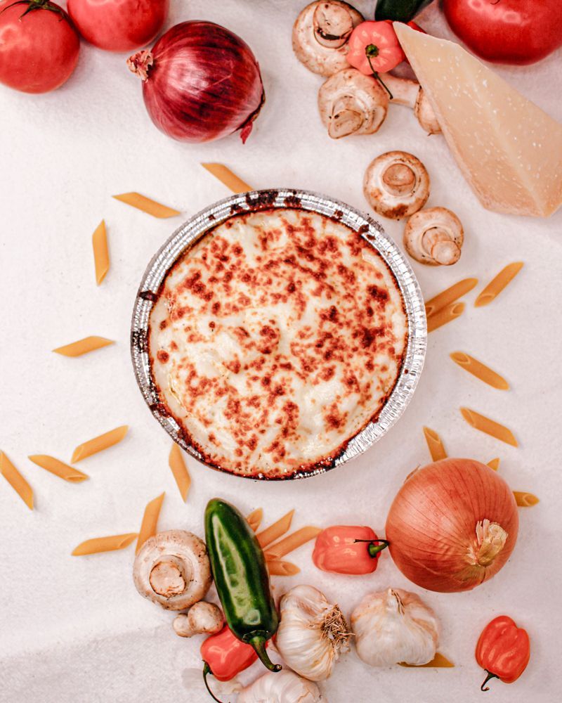 A pizza is surrounded by vegetables and pasta on a table.