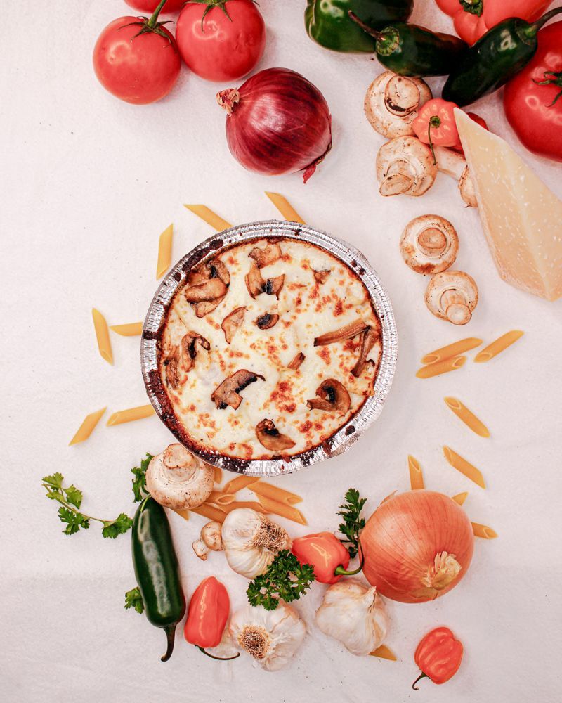 A pizza surrounded by vegetables and pasta on a table.