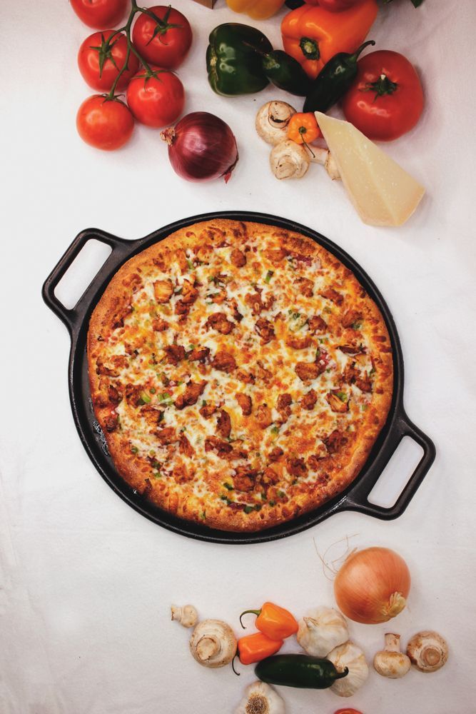 A pizza in a pan surrounded by vegetables on a table.