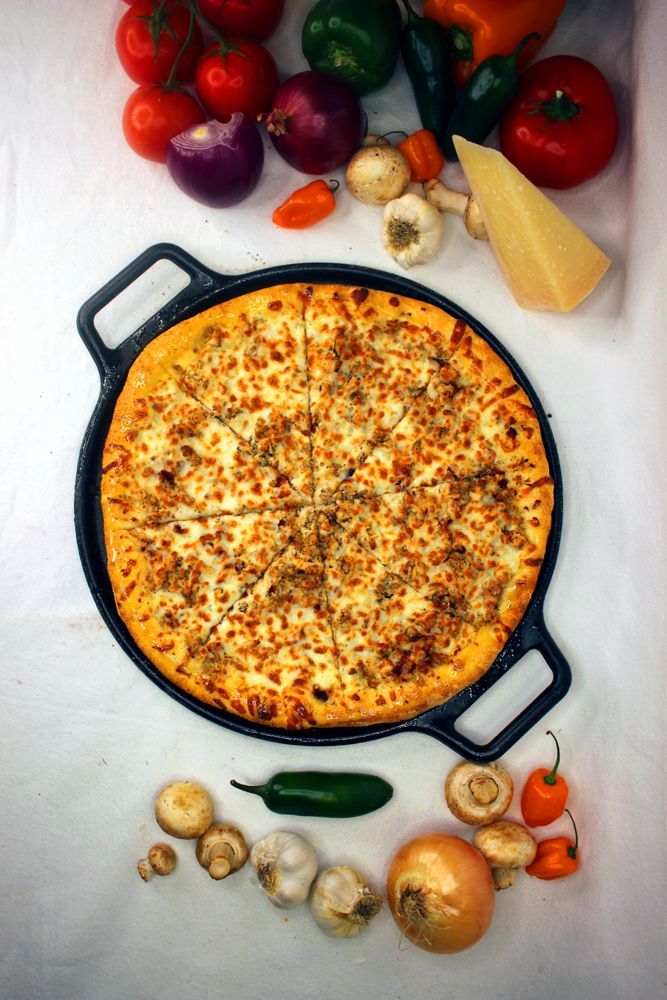A pizza in a pan surrounded by vegetables on a table.
