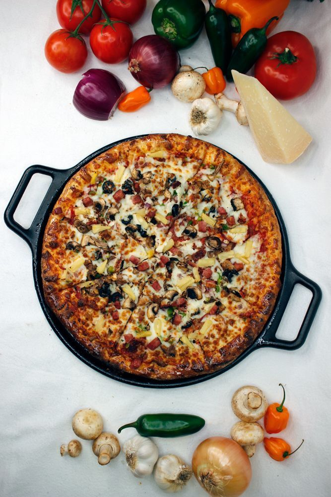 A pizza in a pan surrounded by vegetables on a table