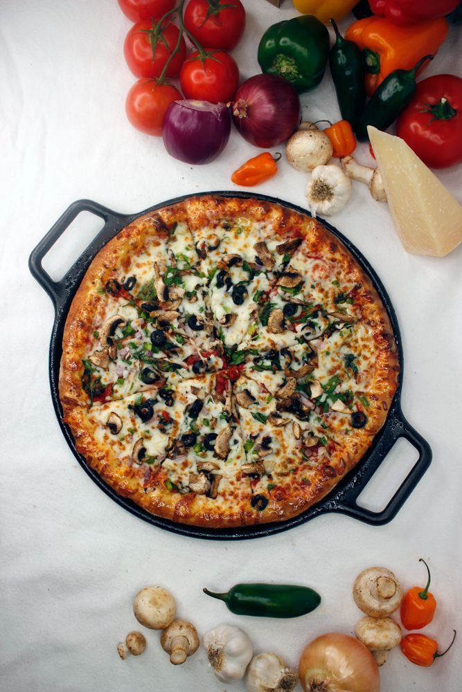 A pizza in a pan surrounded by vegetables on a table