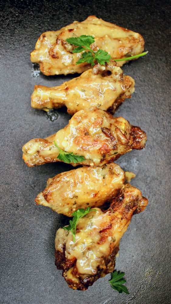 A row of chicken wings with parsley on a black plate.