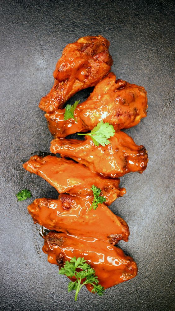 A stack of chicken wings with sauce and parsley on a black plate.
