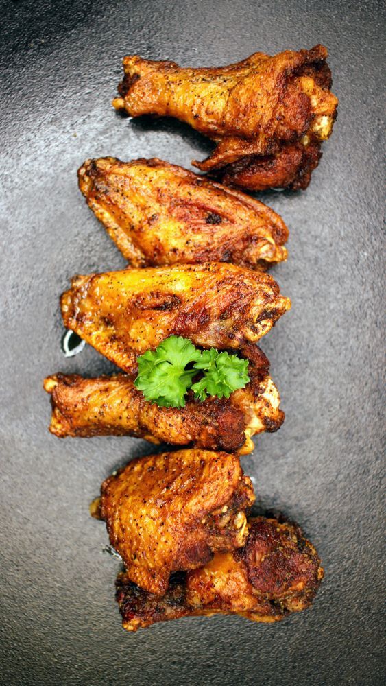 A row of fried chicken wings with parsley on a black plate.