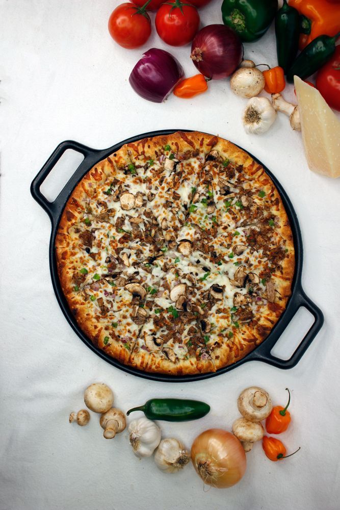 A pizza is sitting in a pan on a table surrounded by vegetables.