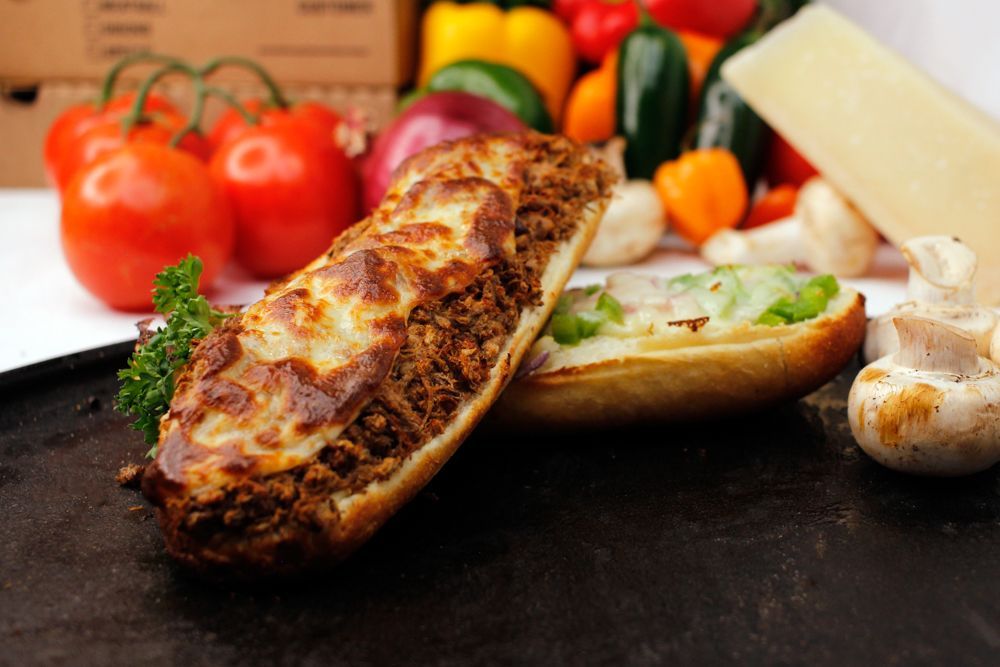 A sandwich with meat and cheese is on a plate with vegetables in the background.