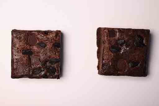 Two brownies with chocolate chips on a white surface.