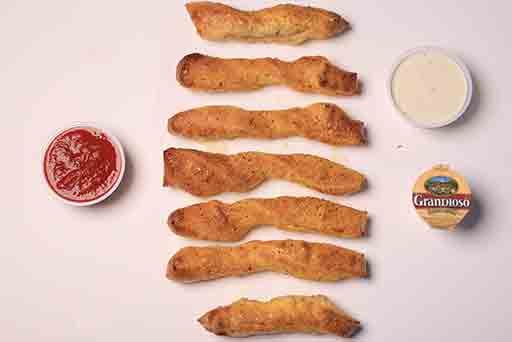 A row of pretzel sticks with dipping sauces on a table.
